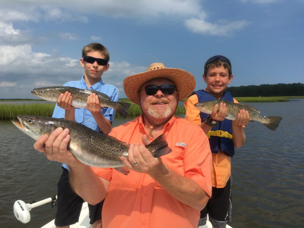 Inshore Fishing Charters In Myrtle Beach. Man and kids holding speckled sea trout. Inshore Fishing Charters In Myrtle Beach near me. Man and kids holding speckled sea trout.