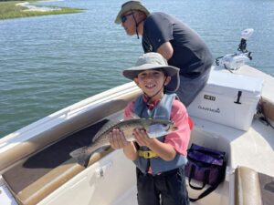 family-friendly-charter-fishing-north-myrtle-beach-sc father and son on the front of bay boat in myrtle beach, south carolina with son holding a speckled sea trout for a family friendly charter fishing