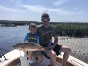 spring-fishing-north-myrtl-beach-redfish-red-drum-sc father and son holding a redfish on the bow of the for Spring Fishing Myrtle Beach with North Myrtle Beach Fishing Charters