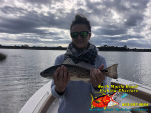Gril holding a red drum aka redfishin the bow of north myrtle beach fishing charters scout bay boat.
